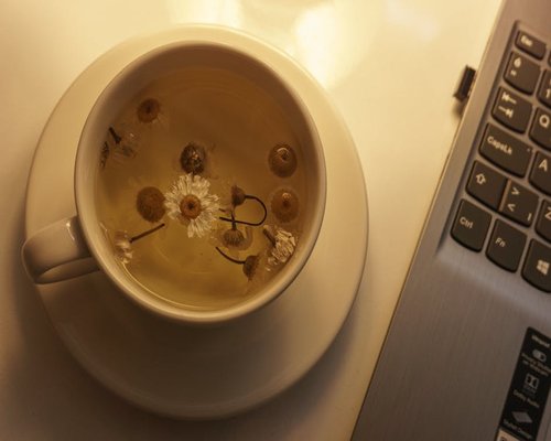 A closed laptop with a cup of herbal tea next to it